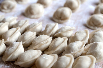 The raw dumplings were placed on a wooden cooking board, sprinkled with flour. The filling is minced meat, potatoes, cheese or cottage cheese. A semi-finished product, ready for cooking.