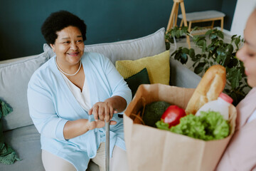 Mature African American female patient rejoicing while she receiving care package from nurse at clinic