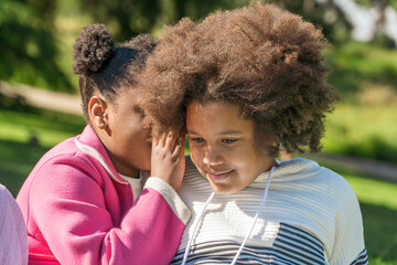 Young girls sharing a secret in a sunny park