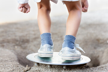 Child standing on a metal shovel on a sandy surface