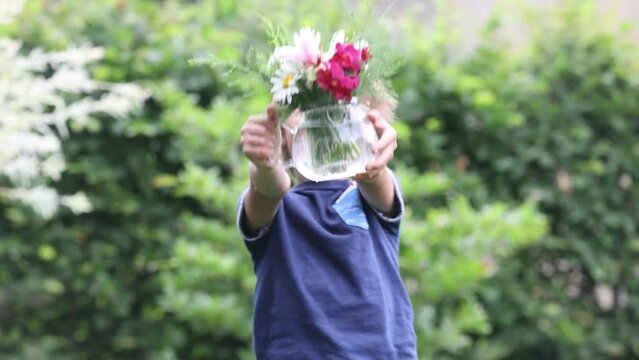 Sweet child, boy, holding vase with fild flowers in garden