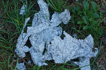 pieces of white crumpled old cellophane lie on the green grass outside