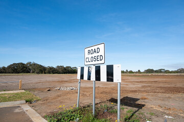 A 'Road Closed' sign stands against a large dirt field in a development area of a new suburban...