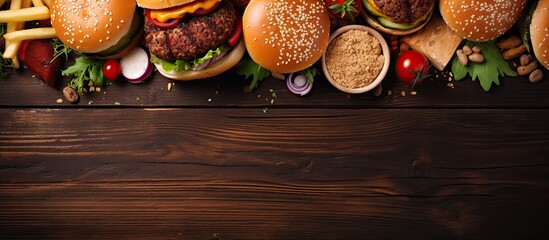 Top view of various takeout or delivery foods like hamburgers, pizza, fried chicken, and sides on a dark wooden background with ample copy space image.
