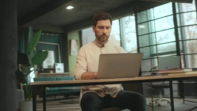Handsome man sitting at desk use laptop and phone in the office. Look serious. Businessman. Camera moving around. 360 Degree