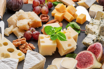 Variety of sliced cheeses with fruits, mint, nuts and cheese cutting knives.