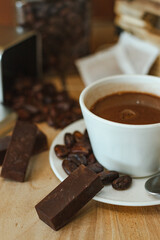 Cocoa bean tea packet in a white glass on a wooden table with chocolate chunks next to it surrounded by seeds.