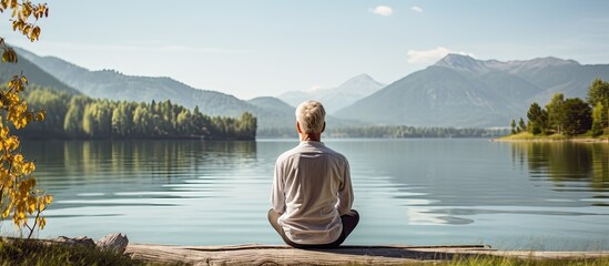 Elderly man practicing yoga by a tranquil lake in a natural setting with copy space image.