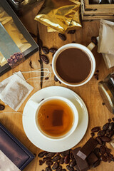 Cocoa bean tea packet in a white glass on a wooden table with chocolate chunks next to it surrounded by seeds.