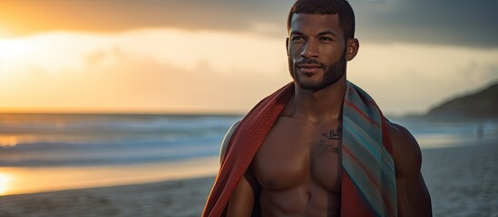 A fit athlete in sports attire with a towel, training by the beach at sunrise, gazes at the sea with copy space image available.