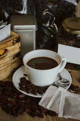 Cocoa bean tea packet in a white glass on a wooden table with chocolate chunks next to it surrounded by seeds.