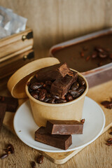 Cocoa bean tea packet in a white glass on a wooden table with chocolate chunks next to it surrounded by seeds.