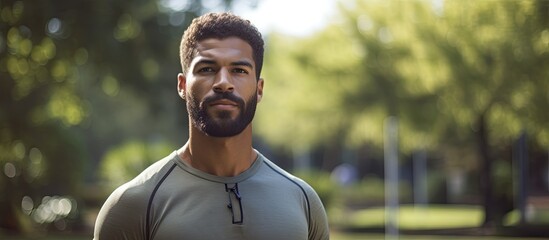Confident young man outdoors in a park, standing for a close-up portrait, ready for a workout, and looking away with copy space image.
