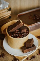 Cocoa bean tea packet in a white glass on a wooden table with chocolate chunks next to it surrounded by seeds.