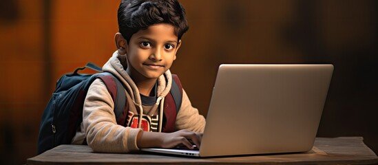 An Indian young boy is pictured using a laptop for an online class in the portrait with copy space image.