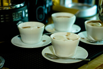 Cocoa bean tea packet in a white glass on a wooden table with chocolate chunks next to it surrounded by seeds.