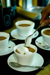 Cocoa bean tea packet in a white glass on a wooden table with chocolate chunks next to it surrounded by seeds.