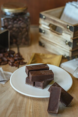 Cocoa bean tea packet in a white glass on a wooden table with chocolate chunks next to it surrounded by seeds.