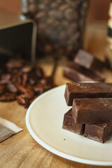 Cocoa bean tea packet in a white glass on a wooden table with chocolate chunks next to it surrounded by seeds.