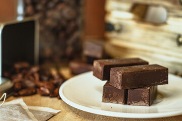 Cocoa bean tea packet in a white glass on a wooden table with chocolate chunks next to it surrounded by seeds.