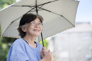 Japanese senior woman holding a parasol on a hot sunny day, to prevent heat stroke in summer and other images. © kapinon