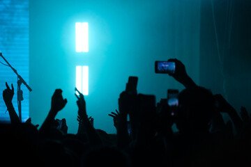 Energetic concert scene with a crowd capturing moments on smartphones, silhouetted against bright...