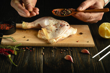 Cooking a chicken leg for dinner by hand on the kitchen table. Adding dry pepper for aroma and special taste.