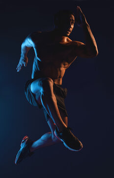Runner, man and fitness in studio with neon light for workout, training and speed for marathon. Healthy, athlete and jump or movement for exercise, cardio and action or fast by dark background