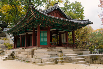 a traditional Korean pavilion with a tiled roof and green window details, set amidst lush trees in Changdeokgung Palace’s Biwon Garden, Seoul.