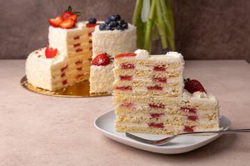 Strawberry and coconut birthday cake with cream and fresh berries. A slice of homemade layered birthday cake. In the background is a bouquet of pink tulips. Selective focus, close-up.