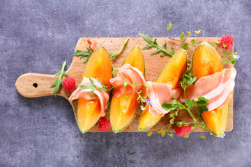 Fresh sweet melon and prosciutto ham on wooden board