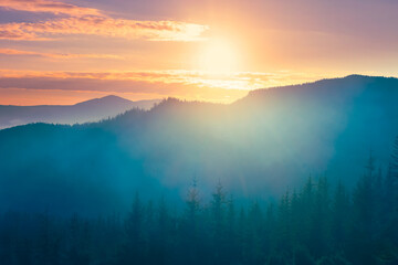 Beautiful sunrise over misty mountain range, with sun shining brightly through clouds. Hills covered in fog blanket, creating a serene and tranquil atmosphere. Travel, tourism, adventure background