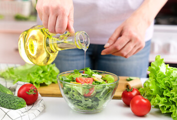 Young woman pouring olive oil in to the vegetable salad. Healthy eating concept.