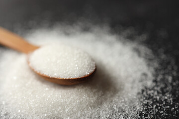 Wooden spoon of sugar top view on black background, splash