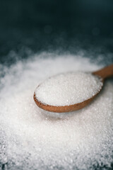 Wooden spoon of sugar top view on black background, splash