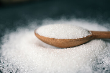 Wooden spoon of sugar top view on black background, splash