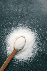 Wooden spoon of sugar top view on black background, splash