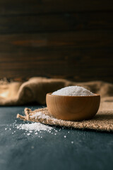Pile of coarse sea salt in wooden bowl on black background