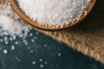 Pile of coarse sea salt in wooden bowl on black background, top view