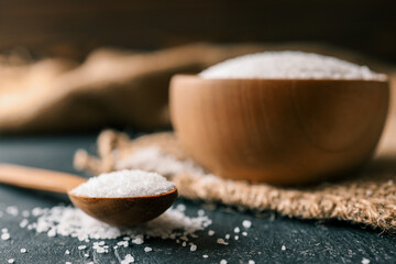 Pile of coarse sea salt in wooden bowl on black background
