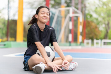 Asian kid girl with a ball sitting on outdoor futsal sports field