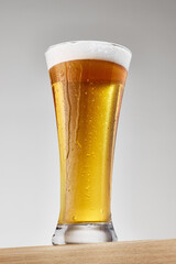 Beer glass with craft, cold, golden, sparkled liquid with frothy, thick, white foam against grey studio background. Concept of food and drink, celebration, Oktoberfest, beverage industry. Ad