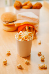 A bucket of popcorn, top-view, warm colors, light brown wooden background, flat lay, daylight macro close-up