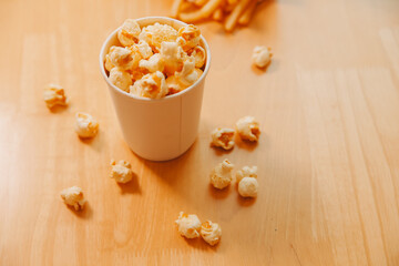 A bucket of popcorn, top-view, warm colors, light brown wooden background, flat lay, daylight macro close-up