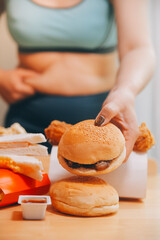 To eat or not. Cheerless plump woman looking at the burger while thinking to eat it or not