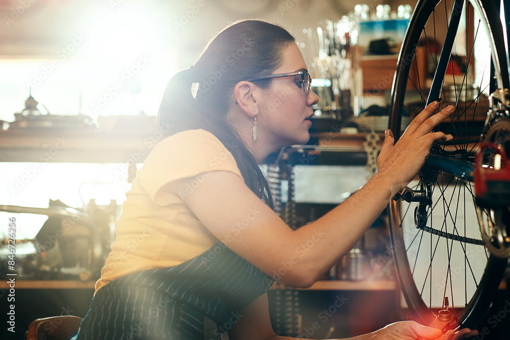 Wall mural Bicycle technician, working and repair in shop with frame, chain and tools for maintenance or cycling. Woman, bike and mechanic in workshop as handyman for gear, inspection and safety with glasses