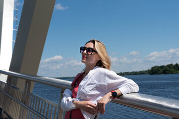 Portrait of a happy girl in sunglasses on a pedestrian bridge over a river in the city