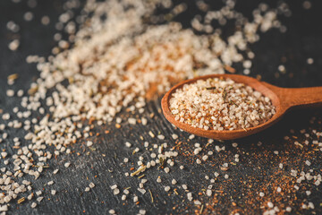 Wooden spoon with sea salt and spices on black background