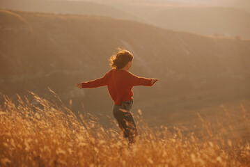 Joyful moment as a woman spreads arms and embraces freedom during a beautiful sunset in a golden...