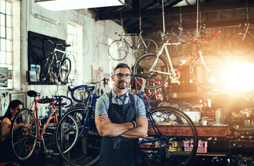 Mechanic, portrait and arms crossed at work in bike repair shop or maintenance garage. Bicycle, man...
